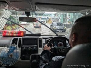 Driver in a car navigating a flooded road during rain, seen from the rear seat.