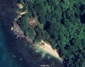 Satellite view of a green, forested island with beach and rocks; clear blue water.