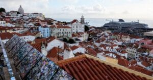 A view from a hill looking down over white houses with red tile roofs. A cruise ship is easily seen, but another is tucked behind it, behind a tower: our ship.