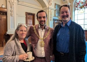 Kit, the Lord Mayor of Belfast, and Randy standing for a photo in an ornate meeting room with carved wood door accents and stained glass windows.