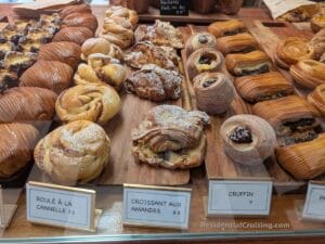 A display of assorted French pastries, each labeled with prices, arranged on wooden boards in a bakery.