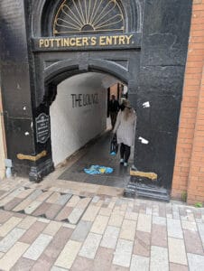 Kit walking ahead of me slips through a low archway, about two people wide, labeled "Pottinger's Entry." in clearly very old metal type. It leads into a narrow street. It was a handy shortcut even when we were not going to any shops there. No concrete or asphalt here: it's all tile walkways and brick walls.