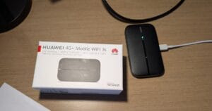 A retail box for a black-colored Hauwei WiFi "mobile hotspot", which is sitting next to it. That little device, about the size of a deck of cards but much thinner, has a USB cable plugged into it for power. It does also have a battery that will run it for 6 hours.
